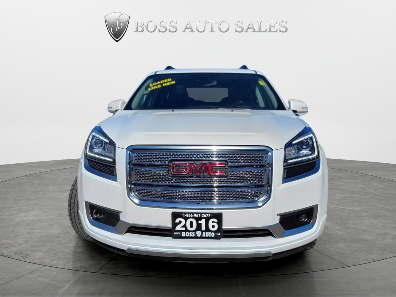 Front view of a 2016 GMC Acadia Denali AWD in white at a dealership, featuring the BOSS AUTO SALES logo above and a "Loaded All Wheel Drive" sticker on the windshield.