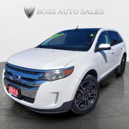 A white 2013 Ford Edge SEL V6 with black alloy wheels is showcased in a showroom under the BOSS AUTO SALES logo. The SUV faces slightly right, featuring a green sticker on its windshield.