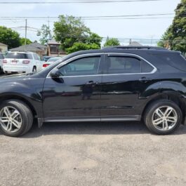 A black 2017 Chevrolet Equinox 2LT AWD is parked on a gravel lot, seen from the side, with other vehicles and trees in the background.