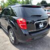 A 2017 Chevrolet Equinox 2LT AWD in black is parked in a lot facing away from the camera, with trees and other cars visible in the background on a sunny day.