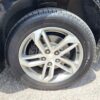 Close-up of a silver alloy wheel and tire on a black 2017 Chevrolet Equinox 2LT AWD, featuring the Chevrolet logo at the center. The vehicle is parked on pavement in bright sunlight.