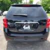 A 2017 Chevrolet Equinox 2LT AWD in black is parked in a lot, rear view shown with dealership contact info on the back window, other vehicles and green trees visible in the background.