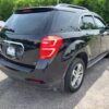 A 2017 Chevrolet Equinox 2LT AWD in black is parked on a gravel lot, shown from the rear left. Other vehicles and green trees appear in the background.