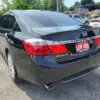 A shiny black 2015 Honda Accord Touring V6 with the LOW KMS license plate is parked in a lot. Trees sway near another white car and some houses in the background.
