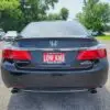 A sleek black 2015 Honda Accord Touring V6 is parked outdoors with a LOW KMS and BOSS AUTO license plate frame. Trees and vehicles surround it, highlighting its elegance in nature.