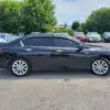 A black 2015 Honda Accord Touring V6 is parked among other vehicles, highlighting its sleek side view. Trees and a house appear in the background under a partly cloudy sky.