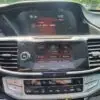 The dashboard of the 2015 Honda Accord Touring V6 features a digital display for radio settings and time, surrounded by AC controls. A start/stop button is on the left, while its sleek design mirrors trees outside.