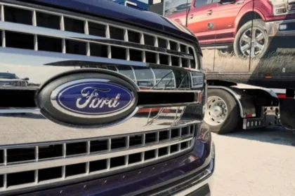 Close-up of a Ford trucks front grille boasting the iconic blue and silver logo. In the background, another truck is partially visible with an image of a red pickup on its side. The scene unfolds outdoors on a sunny day, reflecting Fords enduring commitment amidst conservative pressure. Close-up of a Ford trucks front grille boasting the iconic blue and silver logo. In the background, another truck is partially visible with an image of a red pickup on its side. The scene unfolds outdoors on a sunny day, reflecting Fords enduring commitment amidst conservative pressure.