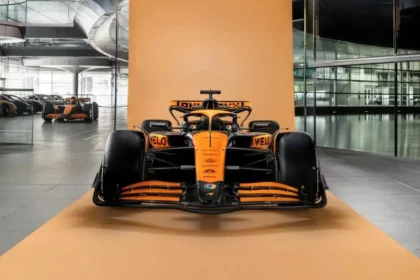 A sleek, orange and black Formula 1 car, reminiscent of those at the F1 Dutch Grand Prix, is displayed on an orange platform indoors. The background features reflective glass walls and another similar car, perhaps paying homage to drivers like Max Verstappen. A sleek, orange and black Formula 1 car, reminiscent of those at the F1 Dutch Grand Prix, is displayed on an orange platform indoors. The background features reflective glass walls and another similar car, perhaps paying homage to drivers like Max Verstappen.
