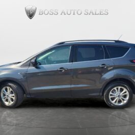 A dark gray 2018 Ford Escape SEL 4WD is shown in profile inside a showroom, parked on a glossy dark floor with the Boss Auto Sales logo visible on the wall behind it.