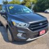 A 2018 Ford Escape SEL 4WD in gray is parked on a paved lot, with Loaded! Mint Condition! in yellow on the windshield. Other cars and green trees are visible under a clear blue sky.