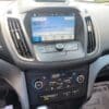 The dashboard of the 2018 Ford Escape SEL 4WD features a touchscreen set to 99.9 FM, framed by media buttons and a CD slot. Below are the AC controls, with the speedometer partly visible on the left and a glimpse of the car seat on the right.