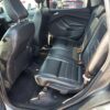 The 2018 Ford Escape SEL 4WD interior features spacious black leather back seats, with an open door allowing natural light to highlight the clean carpeted floor, underscoring its rugged capability.