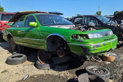 A bright green, stripped-down car, this Junkyard Gem is propped up with missing tires in an outdoor scrapyard. Surrounding it are other vehicles with hoods open and various car parts scattered on the ground, each telling a tale of past glory. A bright green, stripped-down car, this Junkyard Gem is propped up with missing tires in an outdoor scrapyard. Surrounding it are other vehicles with hoods open and various car parts scattered on the ground, each telling a tale of past glory.