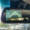 The 2017 Dodge Ram 1500 ST 4X4s rearview mirror shows backup camera footage with parking guidelines in red, yellow, and green, revealing cars along the street as sunlight and reflections dance across this rugged vehicles view.