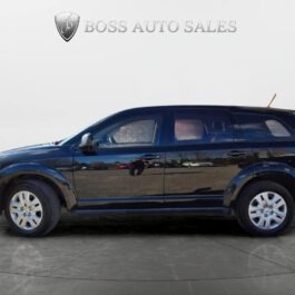 A 2017 Dodge Journey SE is parked indoors on a circular display platform with the Boss Auto Sales logo and text in the background. The vehicle is viewed from the side, displaying all four wheels.