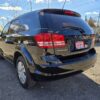 A 2017 Dodge Journey SE, shining under the sun in an outdoor lot, has a Super Clean sign on its back window. Framed by scattered clouds, trees, and power lines against a clear sky, it stands out in the scene.