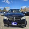 A sleek black 2017 Dodge Journey SE with a blue license plate is parked outside a dealership. Other cars are visible under a clear sky, with Boss Auto and Safs Auto signs in the background.