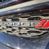The 2017 Dodge Journey SEs front grille showcases the Dodge emblem and red logo on a black mesh that reflects sunlight, highlighting its sleek design.