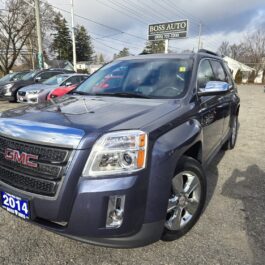 A 2014 GMC Terrain SLT1 in dark blue is parked among other vehicles on a car lot. A Boss Auto sign stands out in the background under a partly cloudy sky.