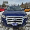 A blue 2013 Ford Edge SEL V6 sits on a snowy lot with colorful vehicles in the background. A Boss Auto sign is visible near a line of trees.