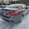 A gray 2018 Nissan Sentra SV with a Gas Saver license plate is parked in a snowy lot, surrounded by other cars and trees.