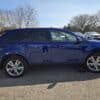 The 2013 Ford Edge SEL V6 in blue, featuring shiny chrome wheels, is parked in a lot on a sunny day. The SUV is viewed from the side with other cars and bare trees visible under a clear sky.