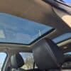 Inside the 2013 Ford Edge SEL V6, the open sunroof frames a clear blue sky. The interior boasts black leather seats with red stitching, while power lines and tree branches are visible through the sunroof.