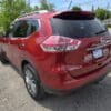 A 2015 Nissan Rogue 2.5 SL AWD in red is parked in a sunny lot, seen from the rear-left with a Loaded dealership plate, trees, and houses visible in the background.
