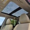 The image shows the interior of a 2015 Nissan Rogue 2.5 SL AWD with beige seats and an open panoramic sunroof, letting in natural light and providing a clear view of the blue sky and power lines outside.