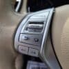 Close-up of the 2015 Nissan Rogue 2.5 SL AWD steering wheel with silver audio and menu control buttons (source, enter, back, volume) on beige leather.
