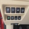 A close-up shows the beige dashboard panel of a 2015 Nissan Rogue 2.5 SL AWD with eight buttons for traction, sport mode, trunk, power door, eco mode, AWD, and hill descent; part of a red door appears on the left.