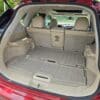 The image shows the spacious trunk of a red 2015 Nissan Rogue 2.5 SL AWD with beige interior, seats folded for extra cargo space, and a ROGUE floor mat, photographed outdoors with greenery in the background.