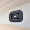 Close-up of a black button with a white open trunk icon, set into the beige interior panel of a 2015 Nissan Rogue 2.5 SL AWD. This button is used to open the trunk on this model.