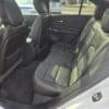 Interior view of a car showcasing the backseat area with black leather seats. Two seats are visible on either side of a middle seat. The cars interior appears clean and spacious, with the front seats partially visible.
