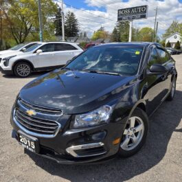 A 2015 Chevrolet Cruze 2LT in black is parked in a car lot under a sunny sky, with other vehicles and a Boss Auto dealership sign visible in the background.