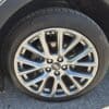 Close-up of a shiny silver alloy wheel and black tire on a 2020 Cadillac XT4 Sport AWD, with the Cadillac emblem at the center, part of a grey fender, and asphalt road visible in the background.