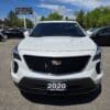 A 2020 Cadillac XT4 Sport AWD in white is parked in a sunny lot, surrounded by other vehicles and trees, with a BOSS AUTO dealership sign visible in the background.