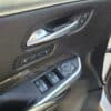 Close-up of a 2020 Cadillac XT4 Sport AWD door interior, featuring the handle, seat memory buttons, window, lock, and side mirror controls with premium black leather and carbon fiber accents.