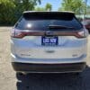 Rear view of a white 2017 Ford Edge SEL parked outdoors on a sunny day, featuring a dealership plate that says LIKE NEW and BOSS AUTO CA, with other vehicles and trees in the background.