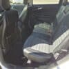 The image displays the back seat of a 2017 Ford Edge SEL, featuring black leather seats and a clean, spacious interior. Sunlight pours in through the open rear door, emphasizing the comfort and well-maintained design of this vehicle.