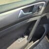 Close-up of a 2015 Volkswagen Golf 1.8T Highline drivers side door panel, showing window and mirror controls, metallic handle, and armrest details highlighted by sunlight.