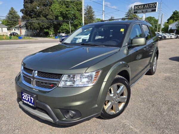 A metallic green 2017 Dodge Journey SUV is parked in a lot in front of a car dealership named Boss Auto, under a clear blue sky. The vehicles front and side are visible, with the headlights off.