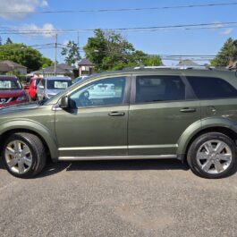 A green SUV is parked in a lot with other vehicles and trees in the background on a sunny day.