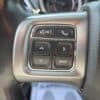 Close-up of the 2017 Dodge Journey Crossroad V6 AWD steering wheel control panel, featuring six buttons for voice recognition, phone, directional arrows, right arrow, and back. The black steering wheel has a textured grip.