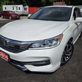 A white 2016 Honda Accord EX-L sedan is parked outdoors in a lot on a sunny day, with other cars and buildings visible in the background.
