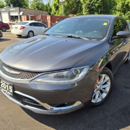 A clean, gray 2015 Chrysler 200 C sedan is parked in a sunny outdoor lot among other vehicles, featuring a front license plate and a windshield sticker.