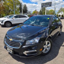 A 2015 Chevrolet Cruze 2LT sedan in black is parked outdoors at a car dealership, with other cars and a BOSS AUTO sign visible in the background beneath a blue, partly cloudy sky.