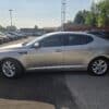 A 2013 Kia Optima EX is parked in a car lot on a sunny day, with other vehicles and trees visible in the background.