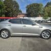 A 2013 Kia Optima EX sedan in silver is parked in a lot on a sunny day, with trees and other vehicles in the background.